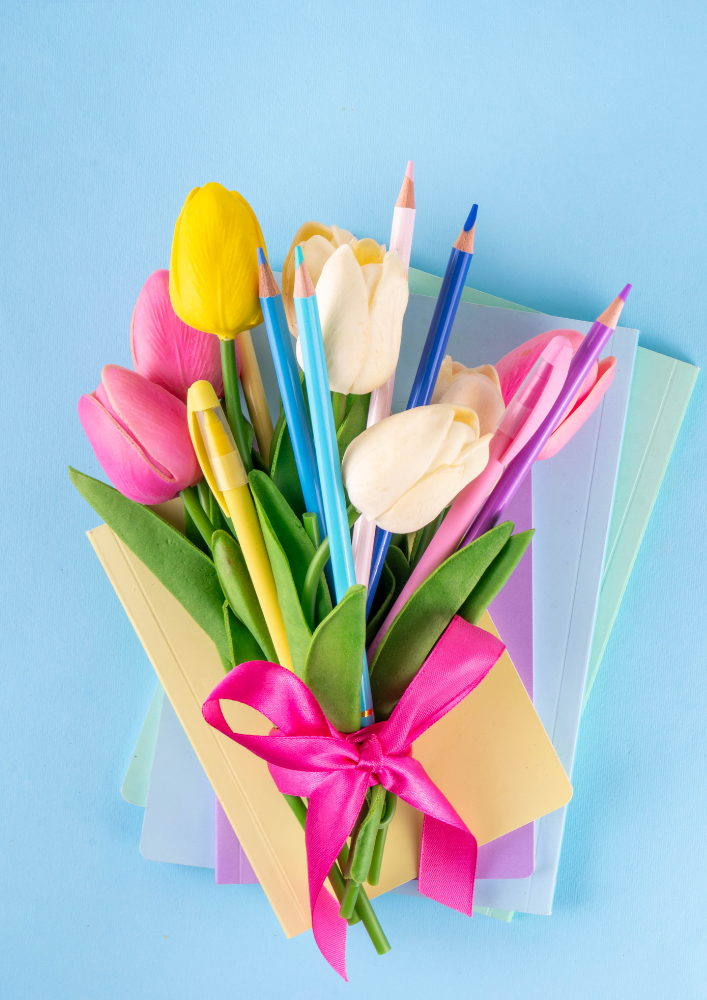 Gift for teacher on blue background featuring brown paper wrapping, rainbow tulips, and pencil crayons — a colourful, heartfelt gesture of appreciation.